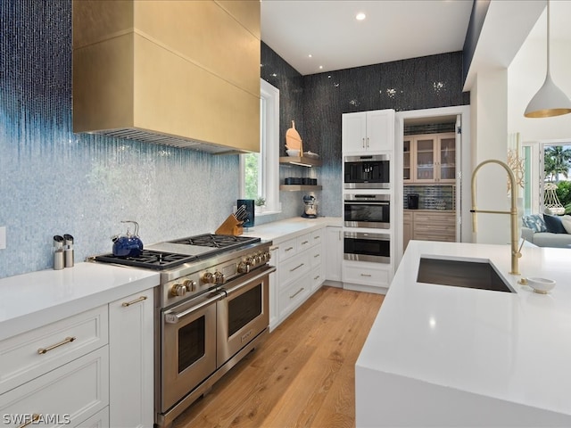 kitchen with sink, light hardwood / wood-style floors, stainless steel appliances, pendant lighting, and white cabinets