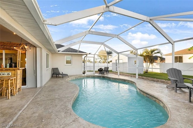 view of swimming pool with glass enclosure, a shed, exterior bar, and a patio