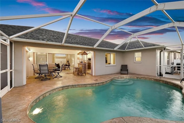 pool at dusk with glass enclosure and a patio area