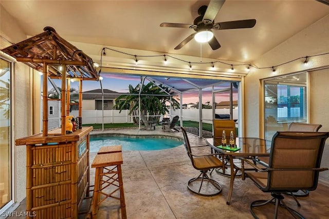 pool at dusk with glass enclosure, ceiling fan, and a patio area