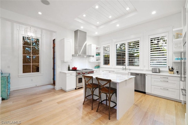 kitchen featuring wall chimney exhaust hood, stainless steel appliances, a center island, a tray ceiling, and white cabinetry