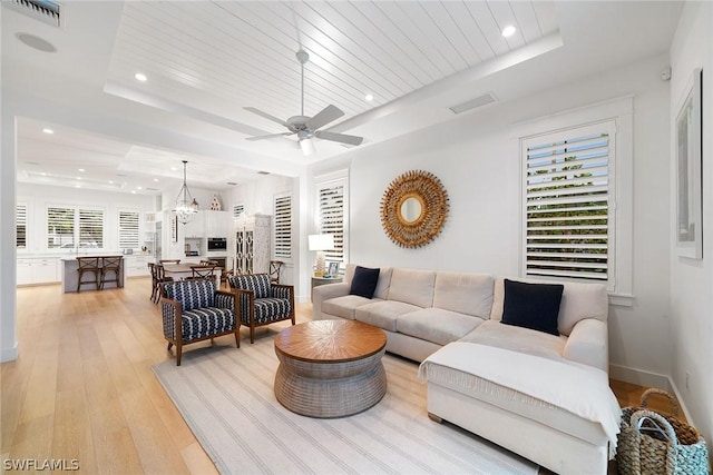 living room with a tray ceiling, ceiling fan with notable chandelier, wood ceiling, and light hardwood / wood-style flooring