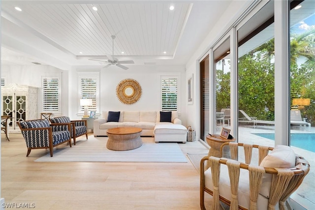 living room with light wood-type flooring, ceiling fan, a tray ceiling, and wood ceiling