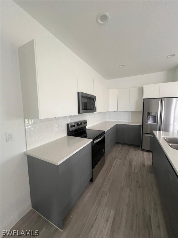 kitchen featuring dark wood-type flooring, sink, decorative backsplash, white cabinetry, and stainless steel appliances