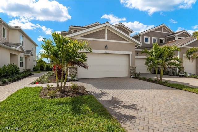 view of front of home featuring decorative driveway, stone siding, a garage, and stucco siding