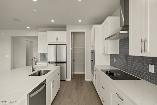 kitchen featuring white cabinets, black appliances, wall chimney range hood, and a sink