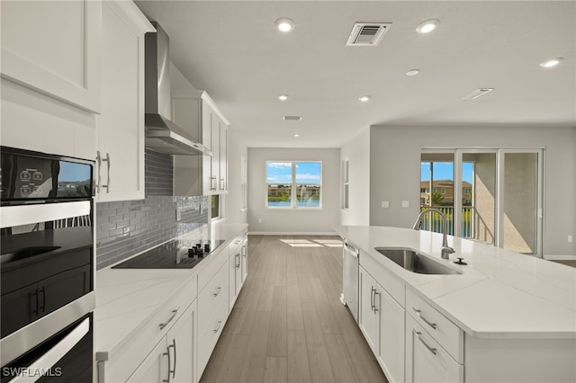 kitchen featuring visible vents, an island with sink, a sink, black appliances, and wall chimney exhaust hood