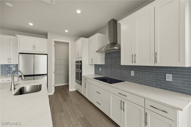 kitchen featuring black appliances, a sink, wood finished floors, white cabinets, and wall chimney range hood