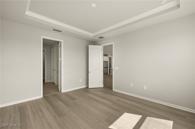 unfurnished bedroom featuring a raised ceiling, wood finished floors, baseboards, and freestanding refrigerator