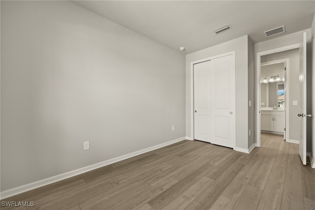 unfurnished bedroom featuring wood finished floors, visible vents, a closet, and baseboards