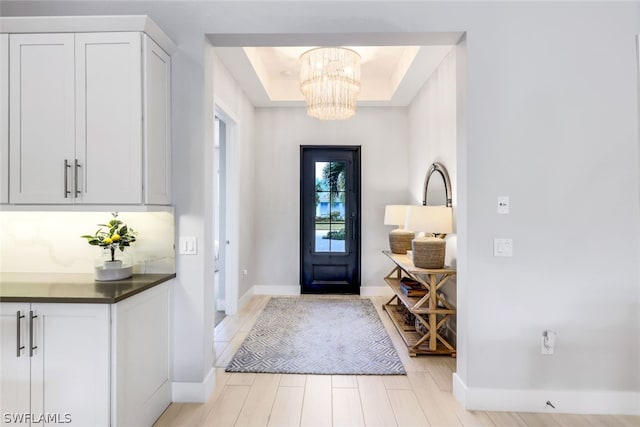 entrance foyer with a chandelier, light wood-type flooring, and a tray ceiling