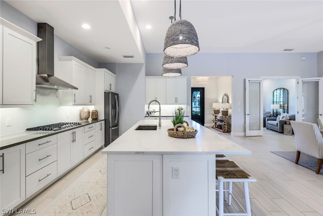 kitchen with sink, wall chimney exhaust hood, stainless steel appliances, decorative light fixtures, and light wood-type flooring