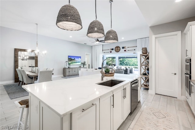 kitchen featuring white cabinets, decorative light fixtures, an island with sink, and sink