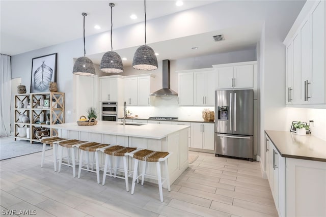 kitchen featuring white cabinetry, a center island with sink, wall chimney exhaust hood, and stainless steel appliances