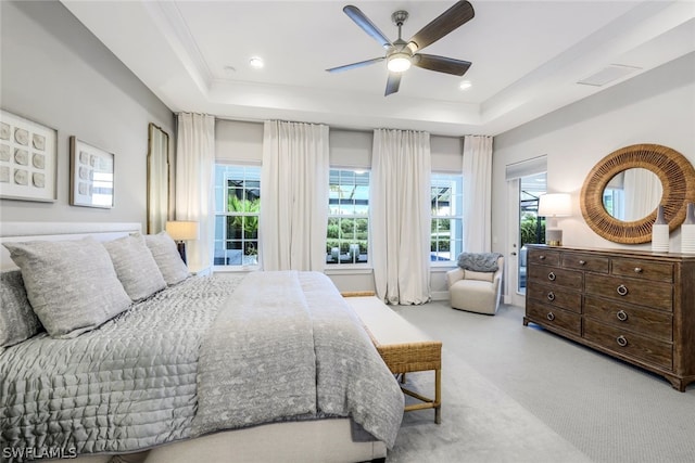 carpeted bedroom with ceiling fan, multiple windows, and a tray ceiling