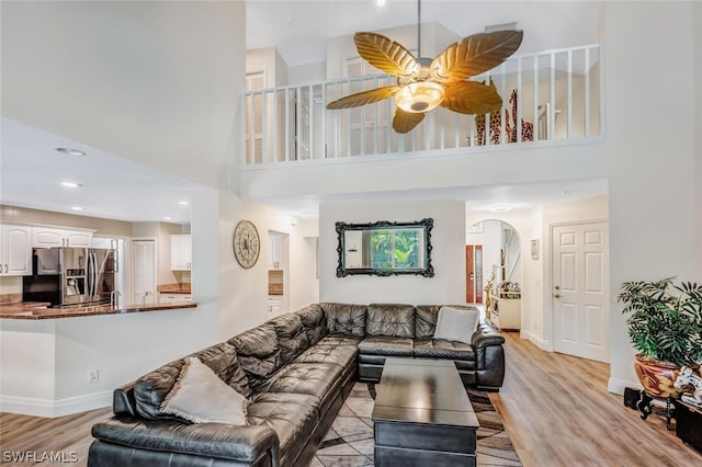 living room with ceiling fan, light hardwood / wood-style flooring, and a towering ceiling