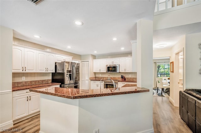 kitchen with white cabinets, stainless steel appliances, light hardwood / wood-style flooring, and dark stone counters