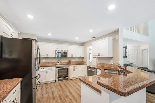 kitchen featuring kitchen peninsula, stainless steel appliances, sink, light hardwood / wood-style flooring, and white cabinetry