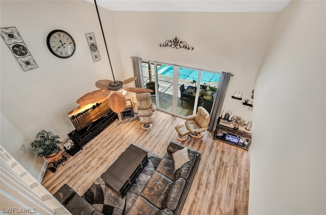 living room with ceiling fan, wood-type flooring, and a towering ceiling