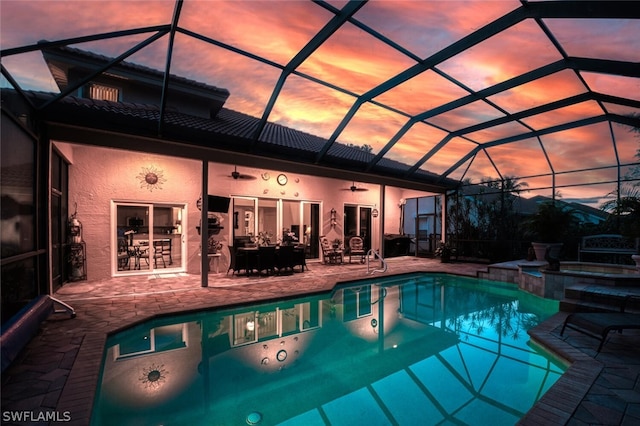 pool at dusk featuring ceiling fan, a patio area, a lanai, and an in ground hot tub