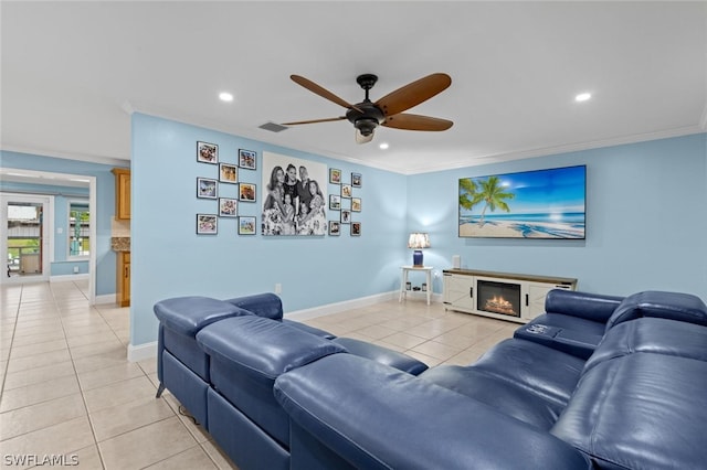 living room featuring ceiling fan, a fireplace, light tile patterned floors, and crown molding