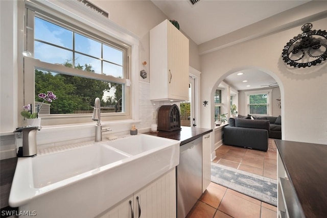 kitchen with backsplash, stainless steel dishwasher, sink, light tile patterned floors, and white cabinetry