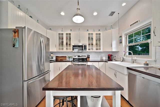 kitchen with decorative backsplash, stainless steel appliances, sink, white cabinets, and hanging light fixtures