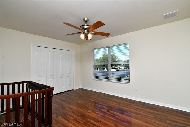 bedroom with a crib, dark hardwood / wood-style flooring, a closet, and ceiling fan