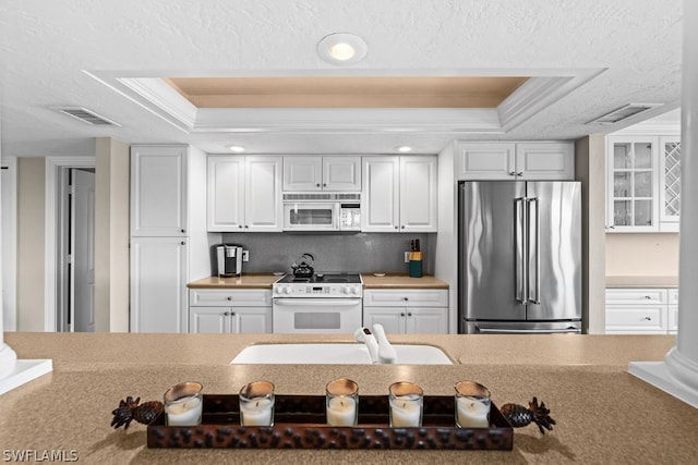 kitchen with a raised ceiling, white cabinetry, sink, and white appliances