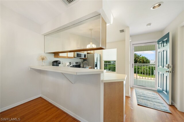 kitchen with light hardwood / wood-style floors, kitchen peninsula, and appliances with stainless steel finishes