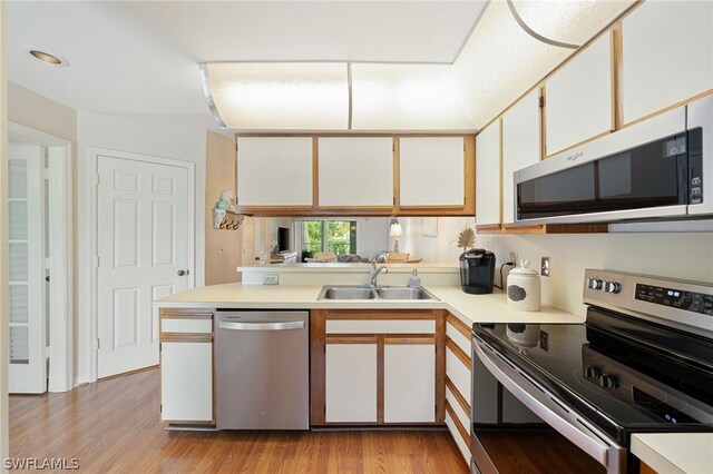 kitchen featuring light hardwood / wood-style floors, kitchen peninsula, white cabinetry, appliances with stainless steel finishes, and sink