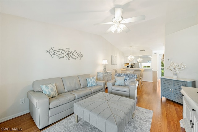 living room with lofted ceiling, wood-type flooring, and ceiling fan with notable chandelier