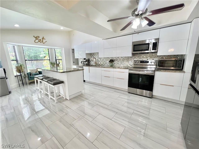 kitchen with a kitchen breakfast bar, backsplash, a center island, white cabinetry, and appliances with stainless steel finishes