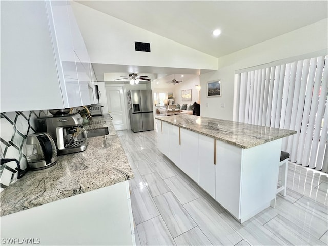 kitchen featuring a kitchen island, ceiling fan, white cabinetry, stainless steel fridge, and lofted ceiling