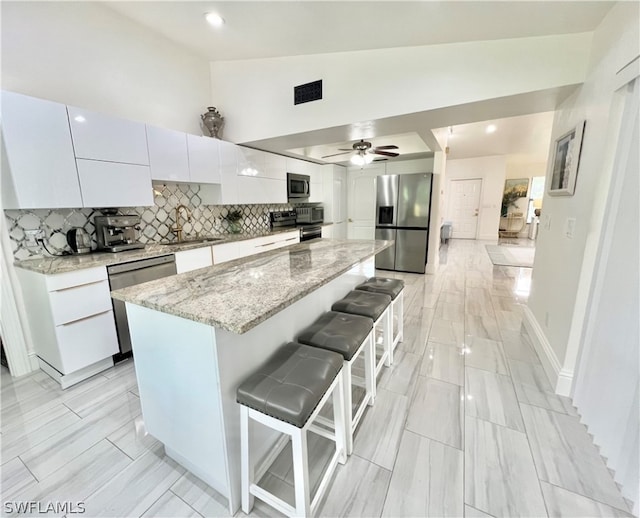 kitchen featuring ceiling fan, tasteful backsplash, a center island, appliances with stainless steel finishes, and a breakfast bar