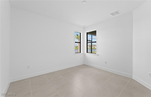 spare room featuring light tile patterned floors, visible vents, and baseboards