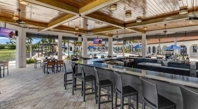 interior space featuring a kitchen bar, coffered ceiling, ceiling fan, light hardwood / wood-style flooring, and beamed ceiling