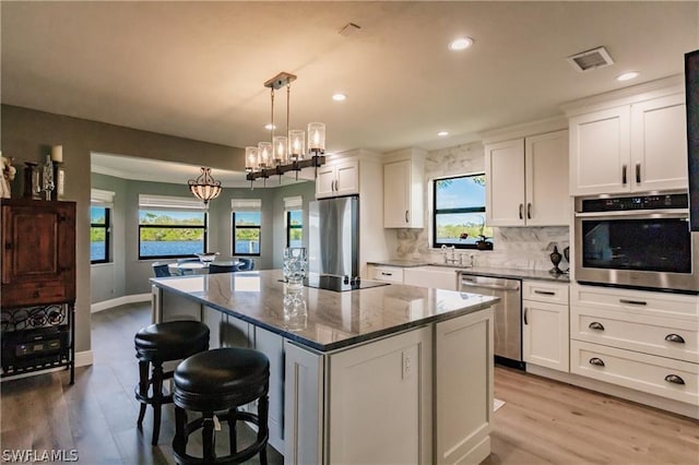 kitchen with appliances with stainless steel finishes, pendant lighting, white cabinets, dark stone counters, and a center island