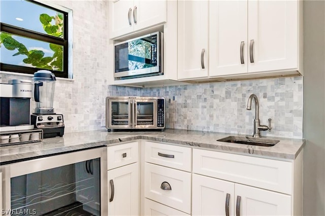 kitchen with light stone counters, beverage cooler, sink, and white cabinets