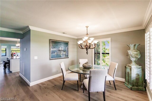 dining area with hardwood / wood-style floors, crown molding, plenty of natural light, and a notable chandelier