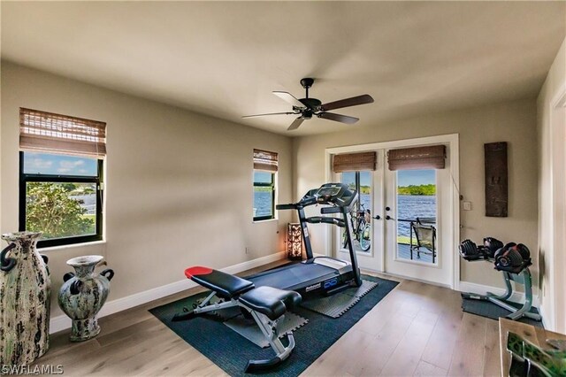 workout room with french doors, hardwood / wood-style flooring, ceiling fan, and a water view