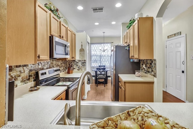 kitchen featuring pendant lighting, tasteful backsplash, sink, stainless steel appliances, and an inviting chandelier