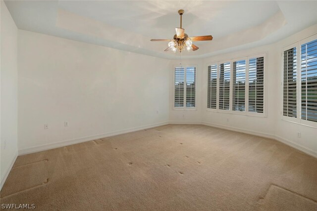 carpeted empty room with ceiling fan, a wealth of natural light, and a tray ceiling