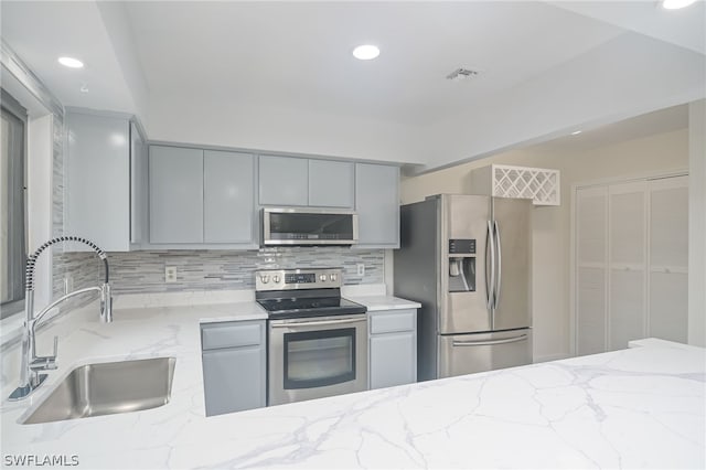 kitchen with gray cabinets, appliances with stainless steel finishes, backsplash, light stone counters, and sink