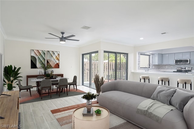 living room featuring light wood-type flooring, ceiling fan, ornamental molding, and sink