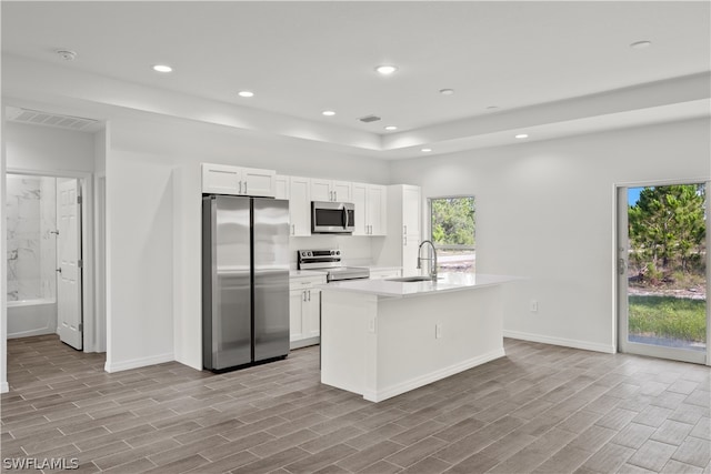 kitchen featuring stainless steel appliances, light wood-type flooring, sink, a kitchen island with sink, and white cabinetry