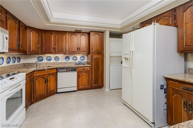 kitchen featuring white appliances, stacked washer and clothes dryer, a raised ceiling, sink, and light stone counters