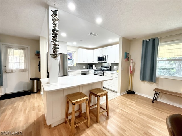 kitchen featuring light hardwood / wood-style floors, a textured ceiling, white cabinetry, appliances with stainless steel finishes, and a breakfast bar area