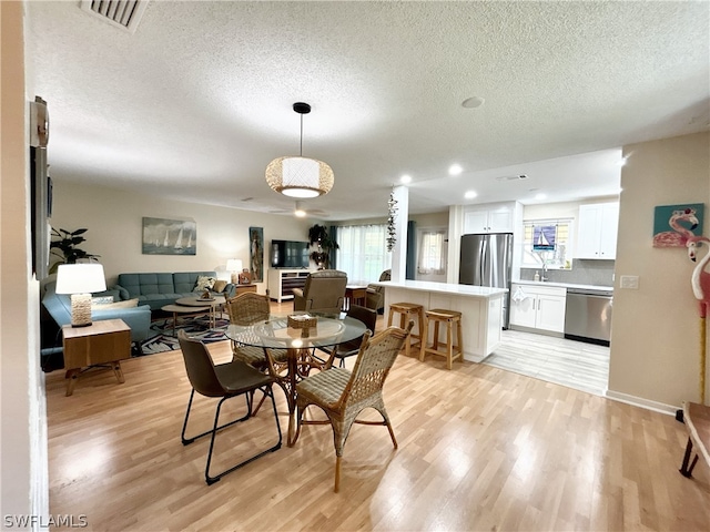 dining area with plenty of natural light, a textured ceiling, and light wood-type flooring