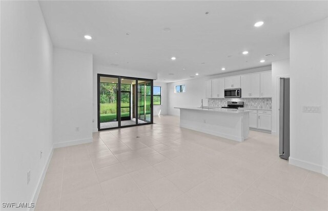 kitchen with appliances with stainless steel finishes, white cabinetry, sink, a center island with sink, and tasteful backsplash